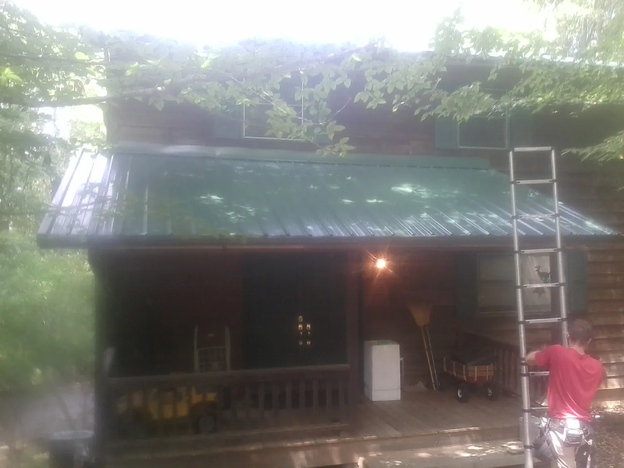 Worker on a ladder at the green porch roof of a wooded cabin in Harmony