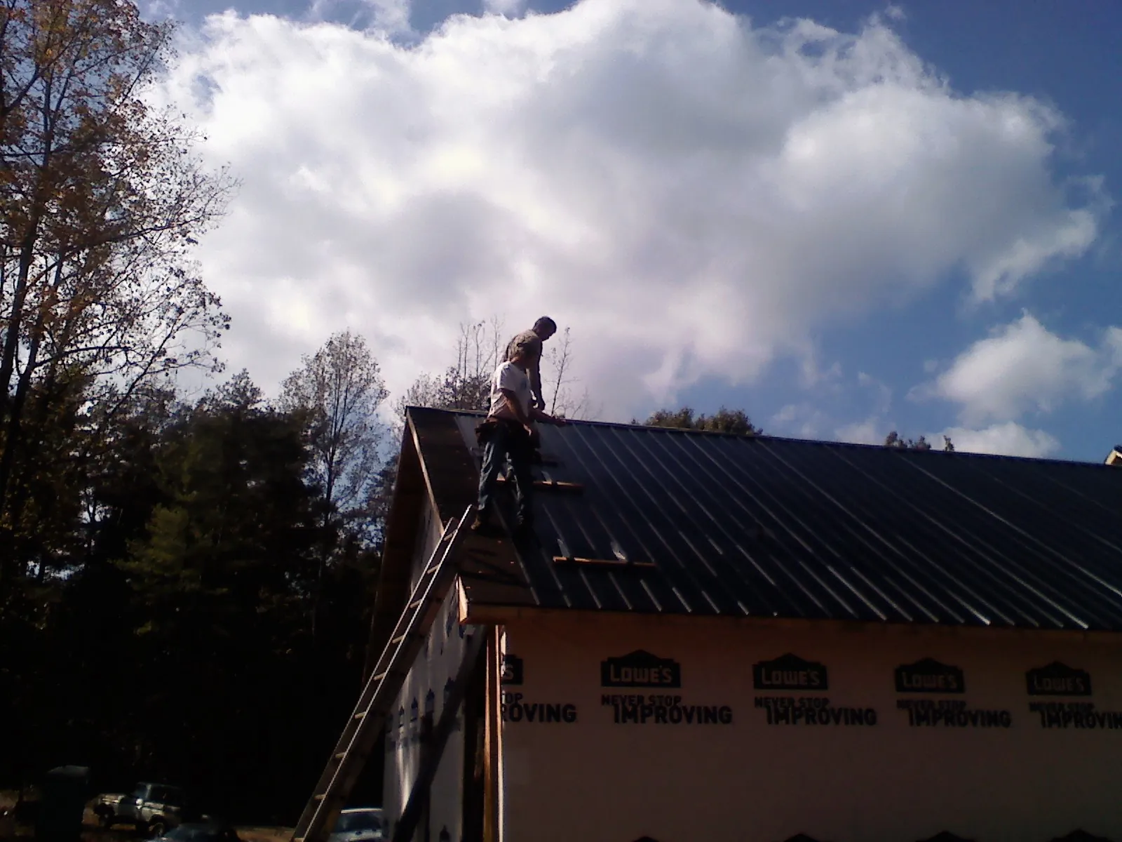 Roofer fastening dark metal panels high against a cloudy sky, from a Roof Inspection job in Harmony