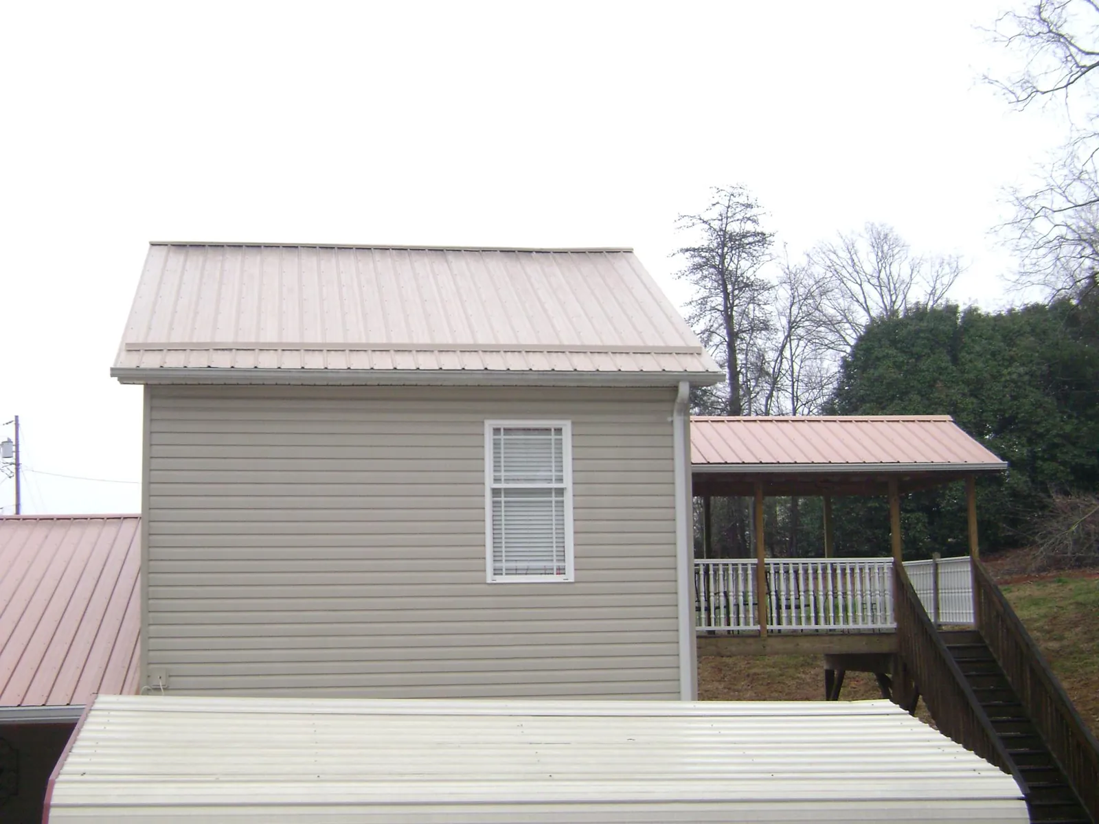 Tan metal roofs on a two story addition and attached porch, from a Roof Replacement job in Harmony